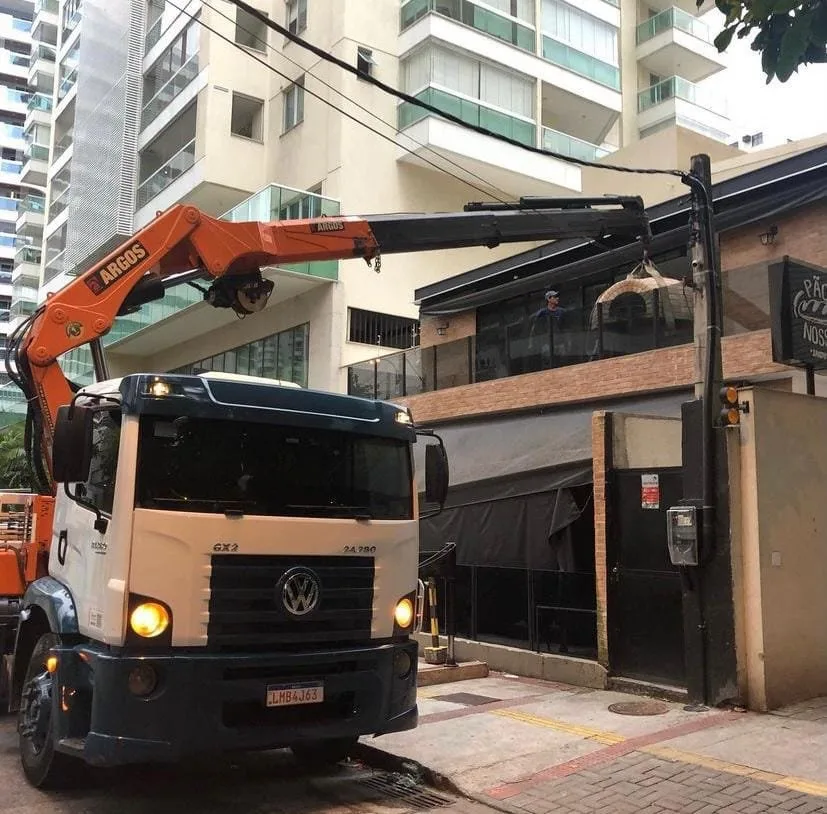 Caminhão munck içando carga na frente de um prédio em rua residencial.