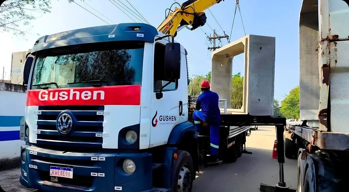 Caminhão munck da Gushen movimentando uma peça pré-moldada de concreto, com operador de capacete ao lado.